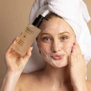 Woman applying Banana Balance Cleanser with a towel on her head against a beige background