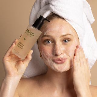 Woman applying skincare product with a towel on her head against a beige background